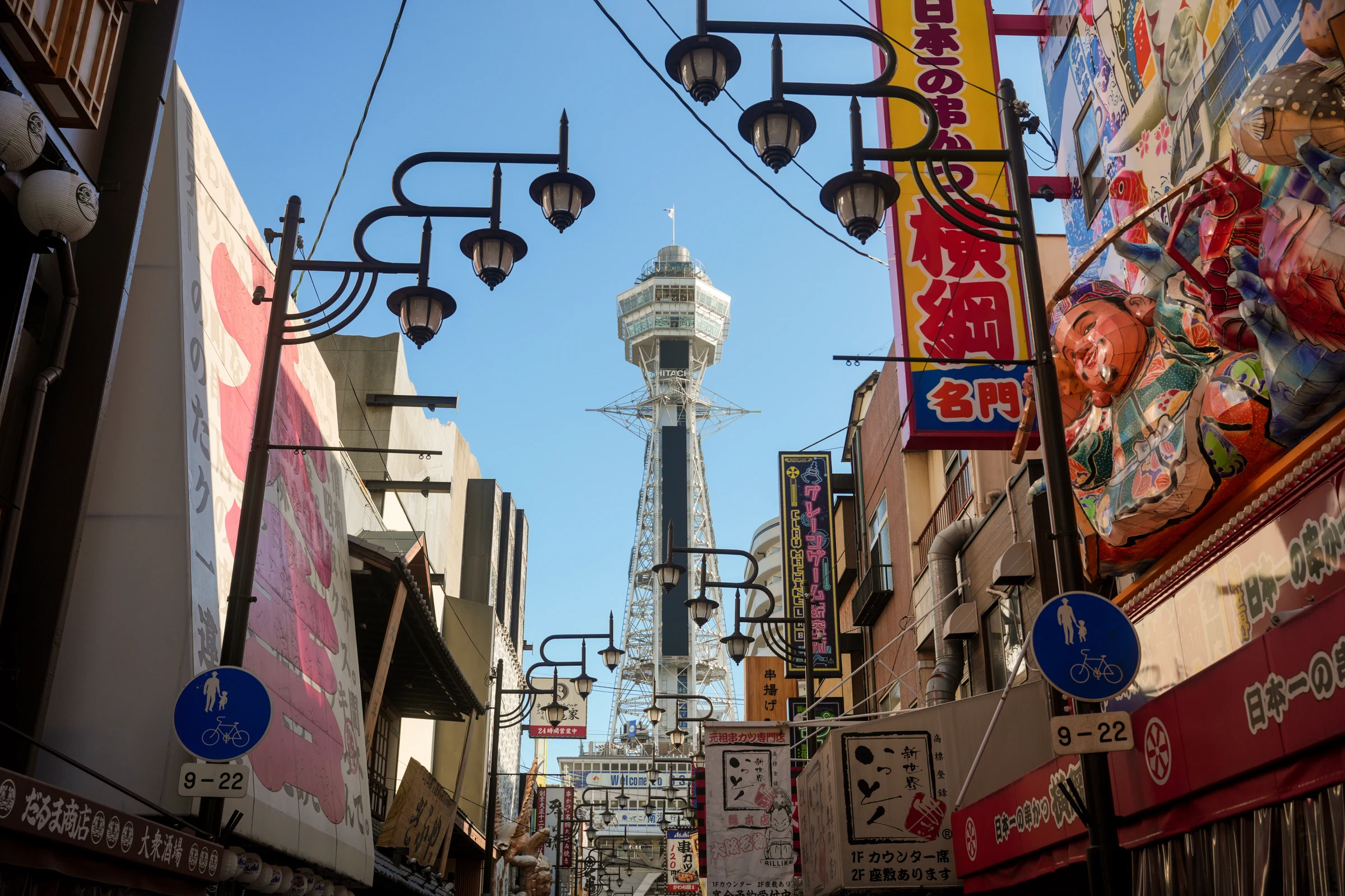 Street signs and lanterns frame a tower against blue sky.